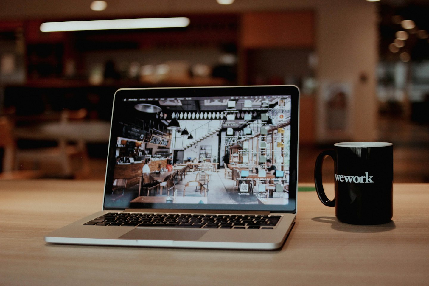 Strieborný notebook a hrnček WeWork na drevenom stole.